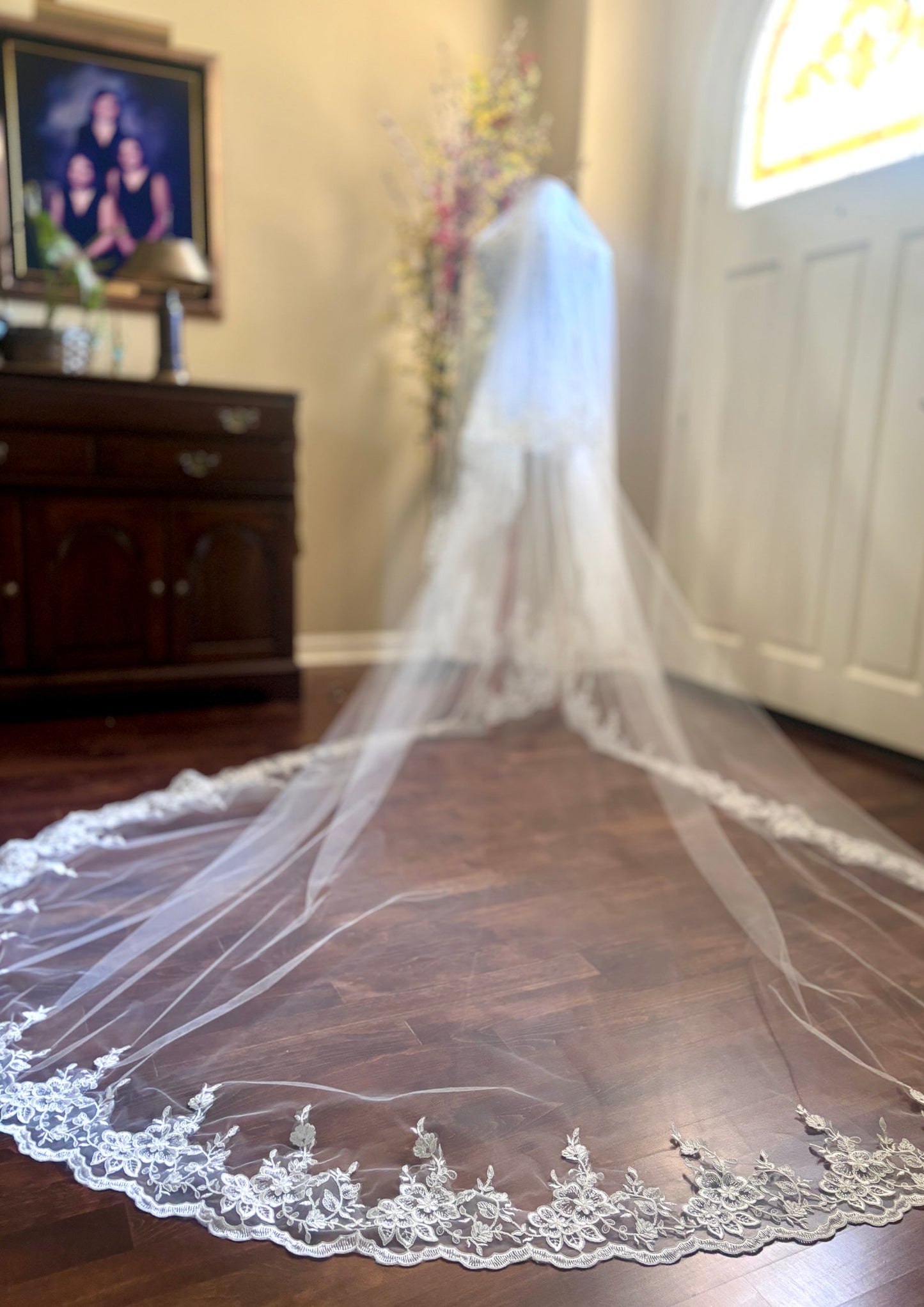 Long white cathedral wedding veil with lace and blusher on a wooden floor.