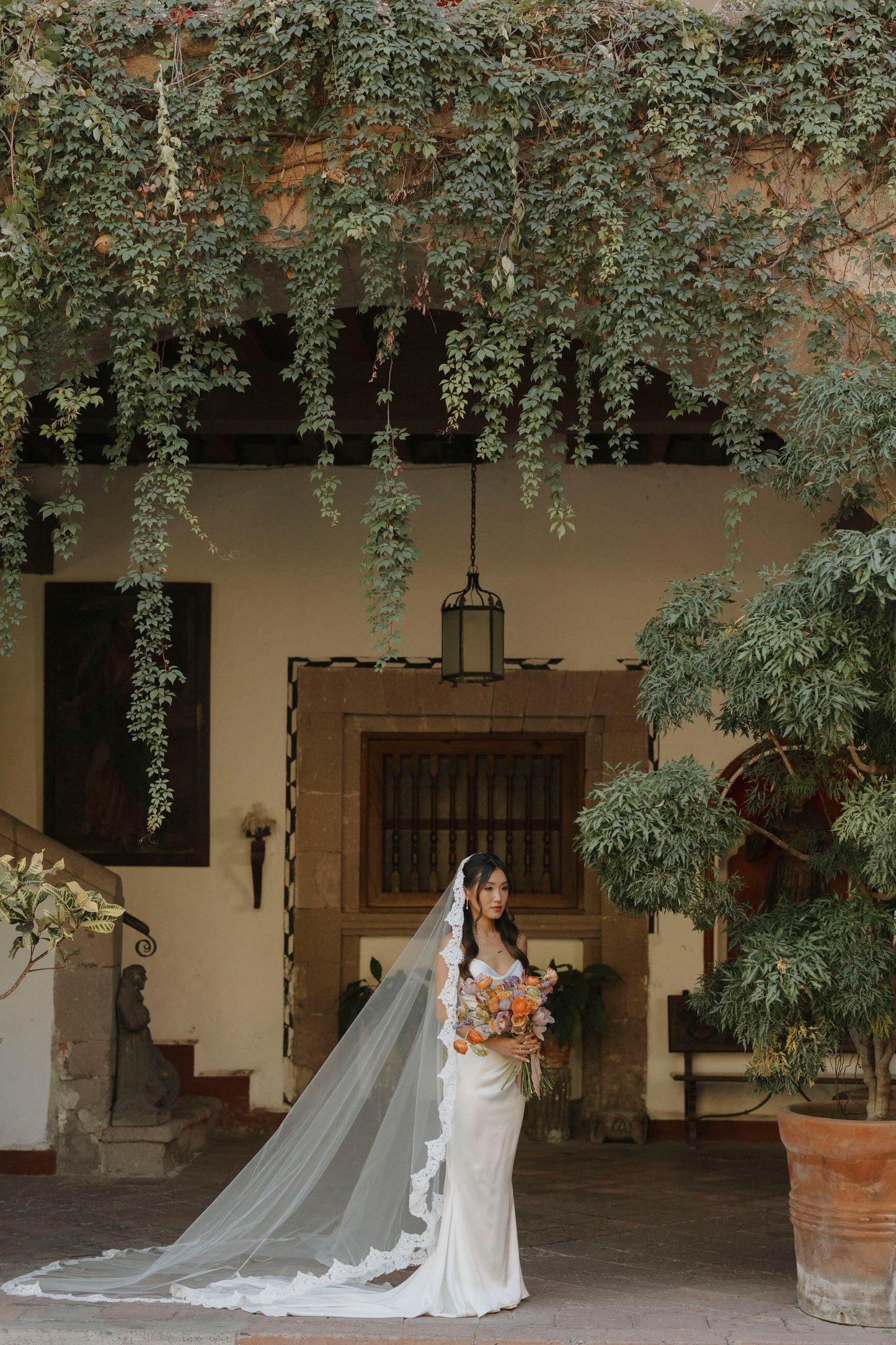 romantic long scallop wedding veil with lace trim on bride holding orange bouquet in Mexico villa