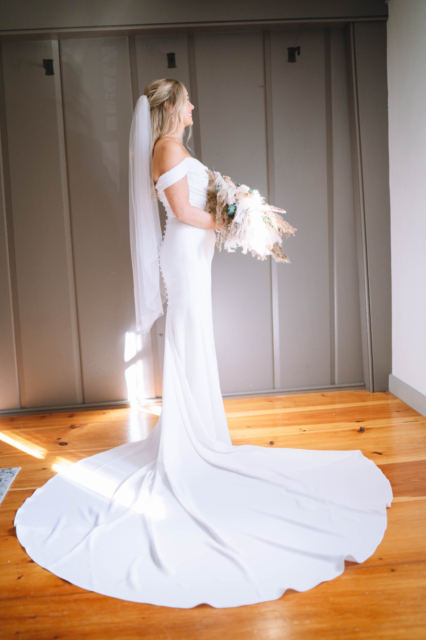 bride in a white ruched wedding dress holding a bouquet wearing fingertip simple veil