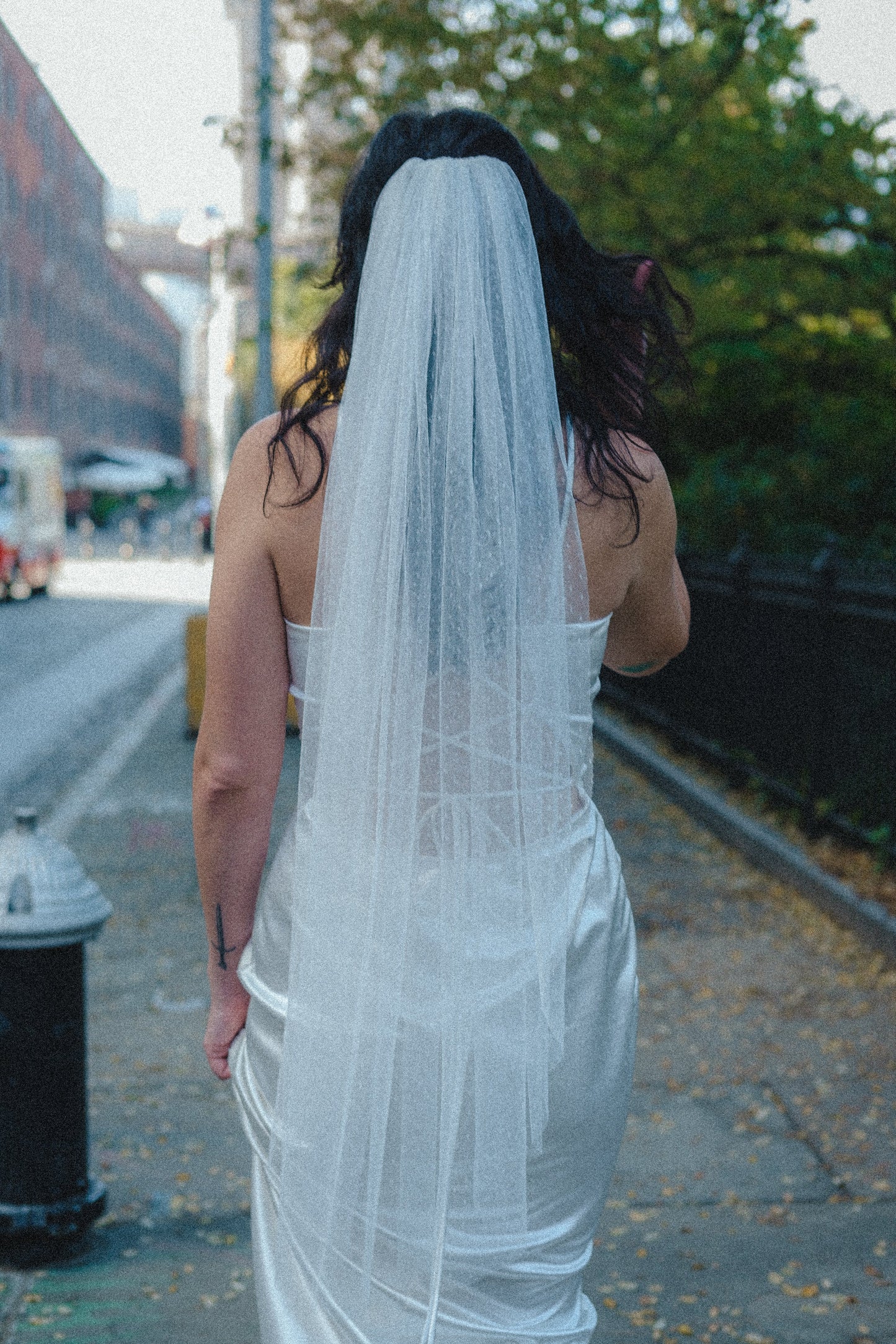 point d' esprit fingertip length bridal veil on scrappy satin slim sheath dress as bride walks through New York City