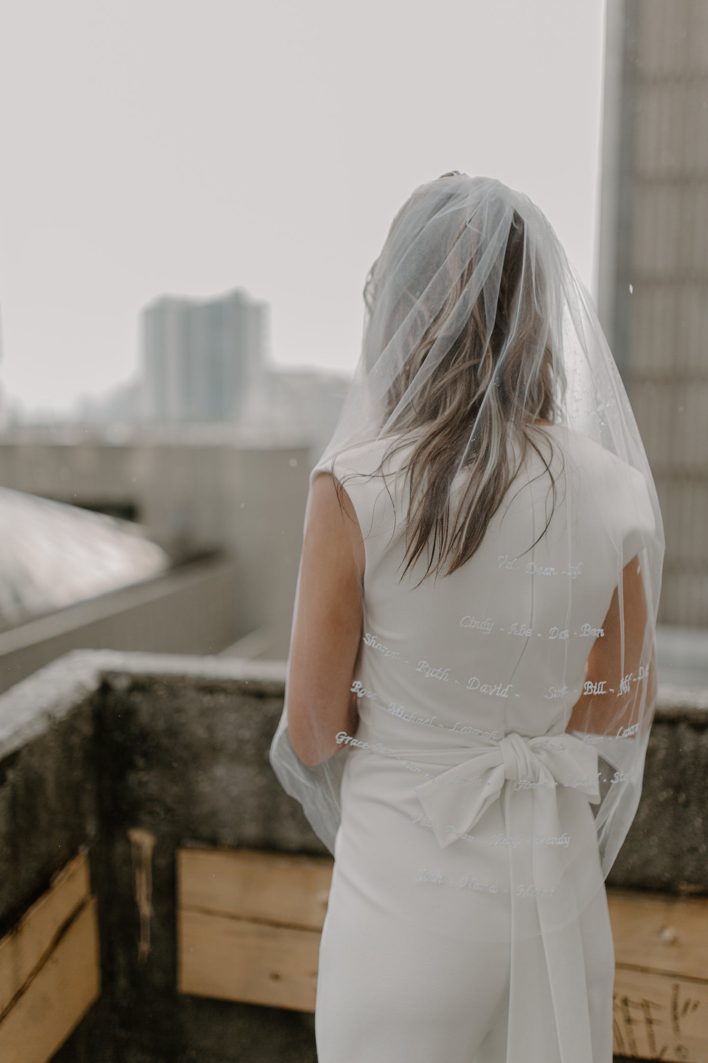bride as she wears fingertip length wedding veil with names and simple bow sash