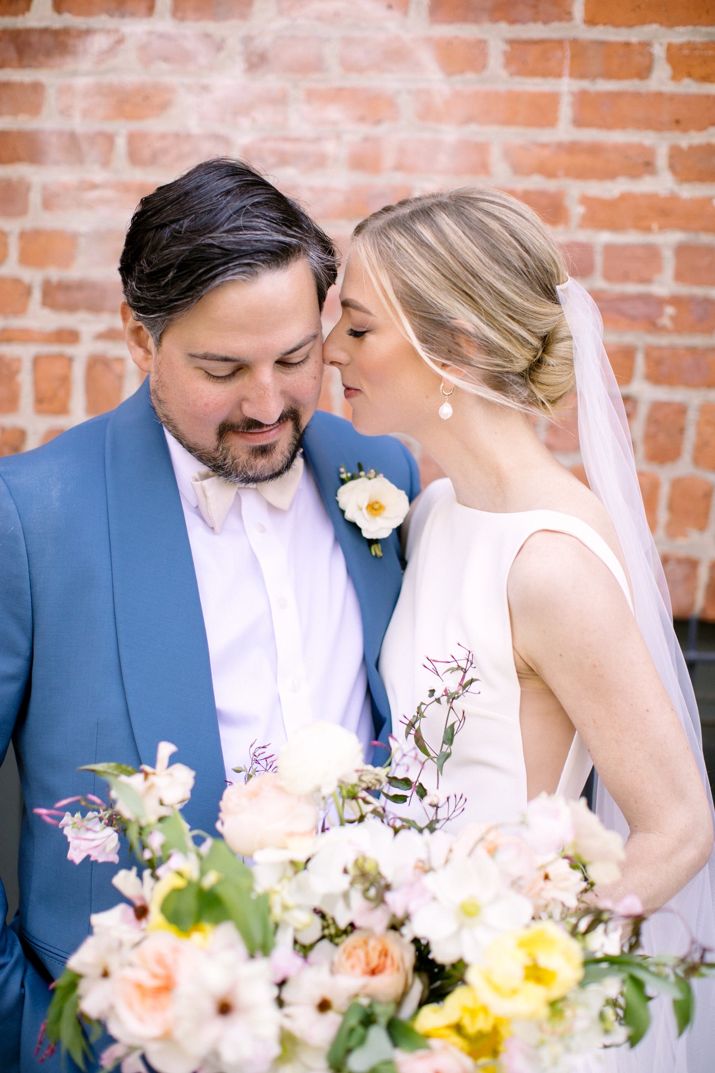 simple minimalist sheer white wedding veil over bride's low twist bun as she embraces groom in navy suit