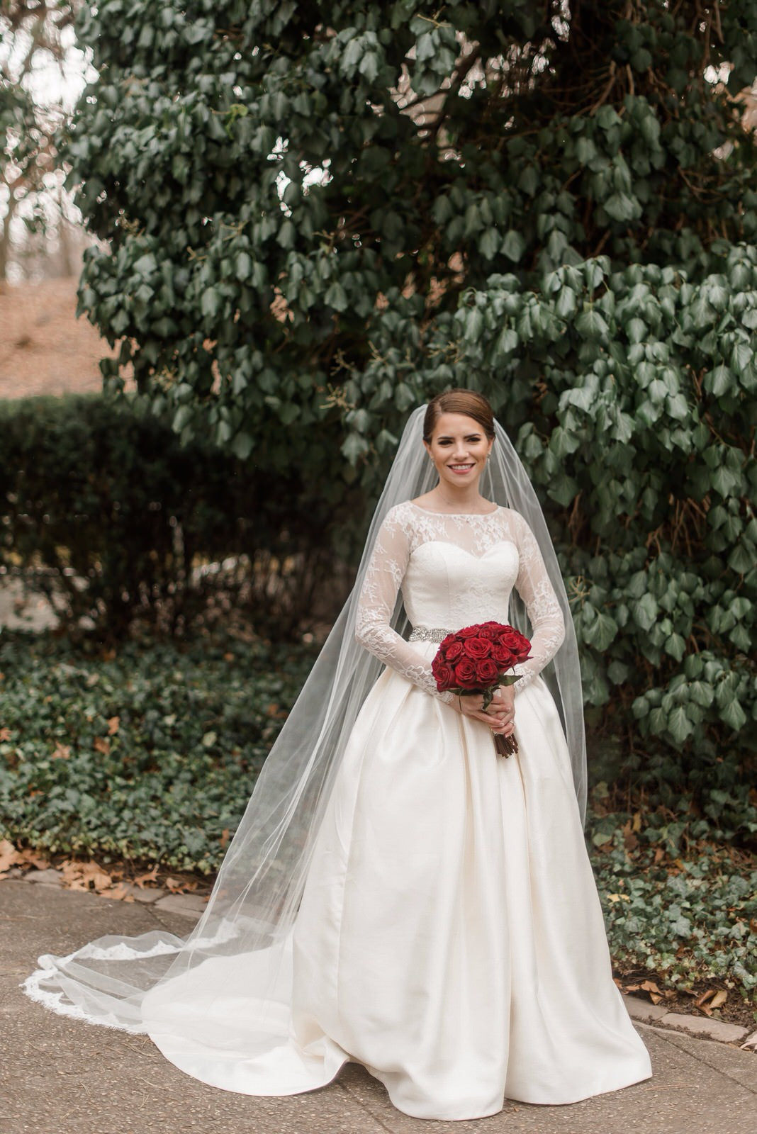 romanti winter bride in long sleeved dress and eyelash lace cathedral veil holding red rose bouquet
