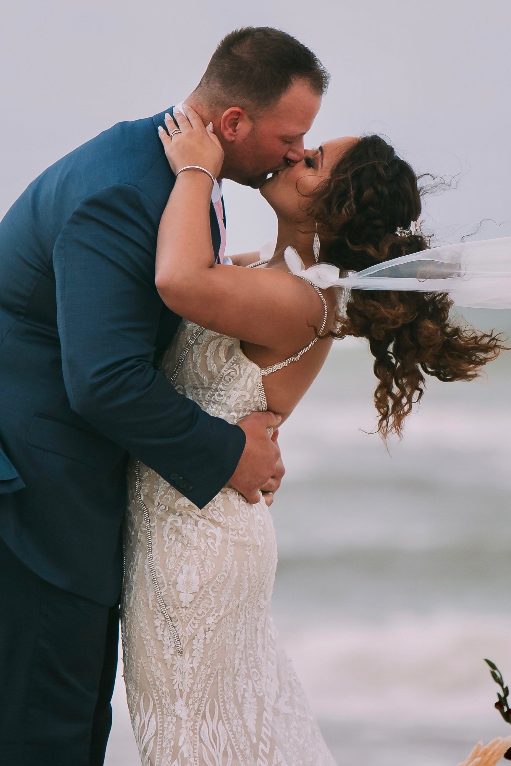 tulle shoulder bow sleeves blowing in wind as bride and groom kiss on the beach