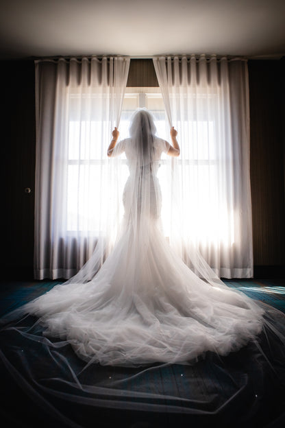 formal royal length scattered crystals wedding veil with dramatic mermaid bridal gown on bride looking out window
