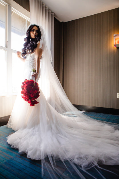 long cathedral length two layer wedding veil on bride holding red rose bouquet