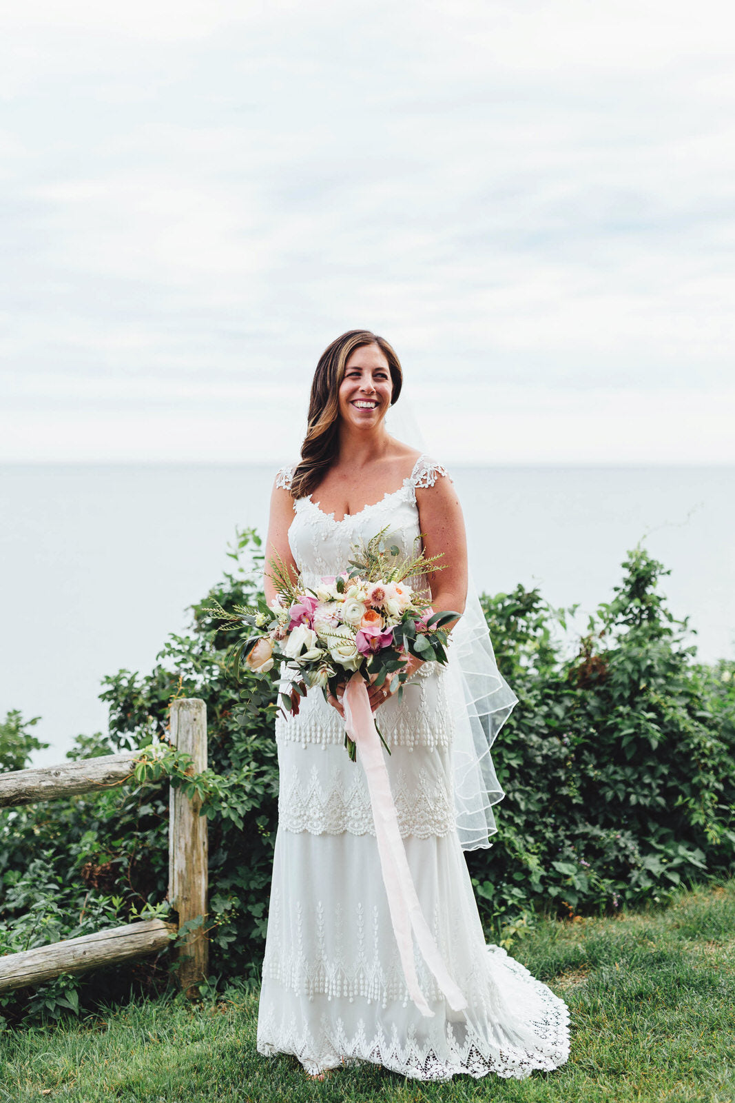 boho bride on cliffside with pink floral bouquet wearing a fingertip length wedding veil  with ribbon edge