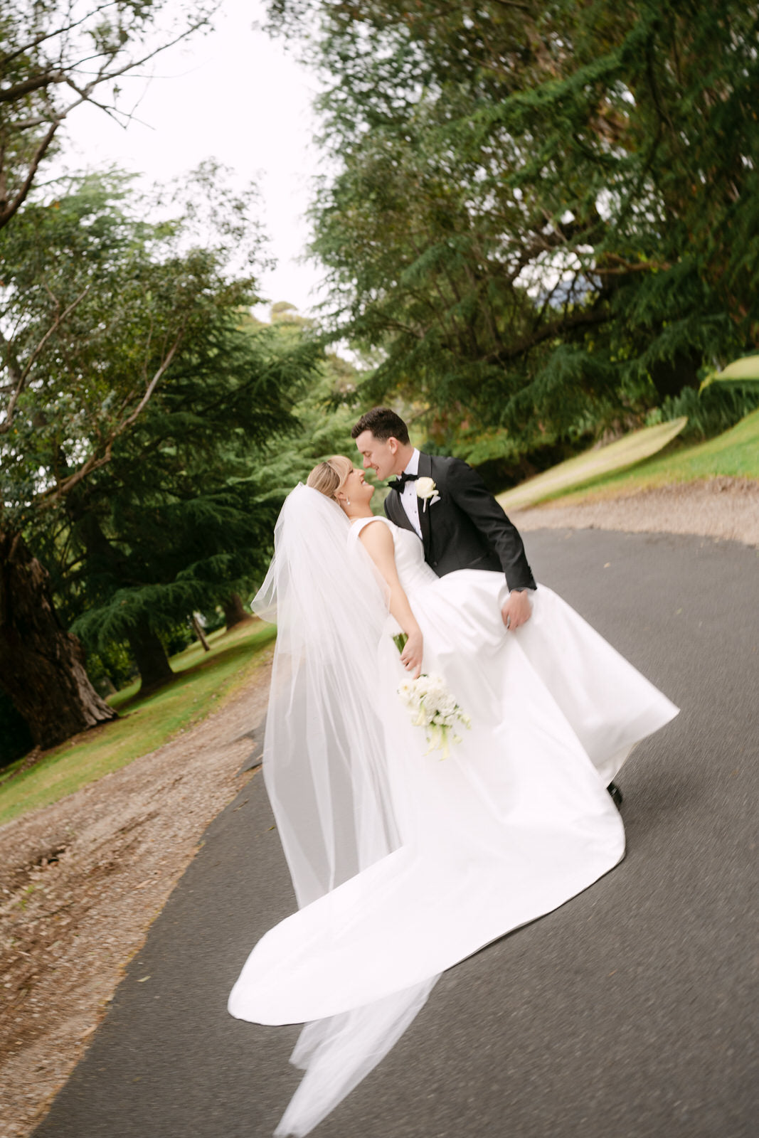 Wedding couple walking together on a path with bride in extra full puffy two layer cathedral wedding veil in off white tulle