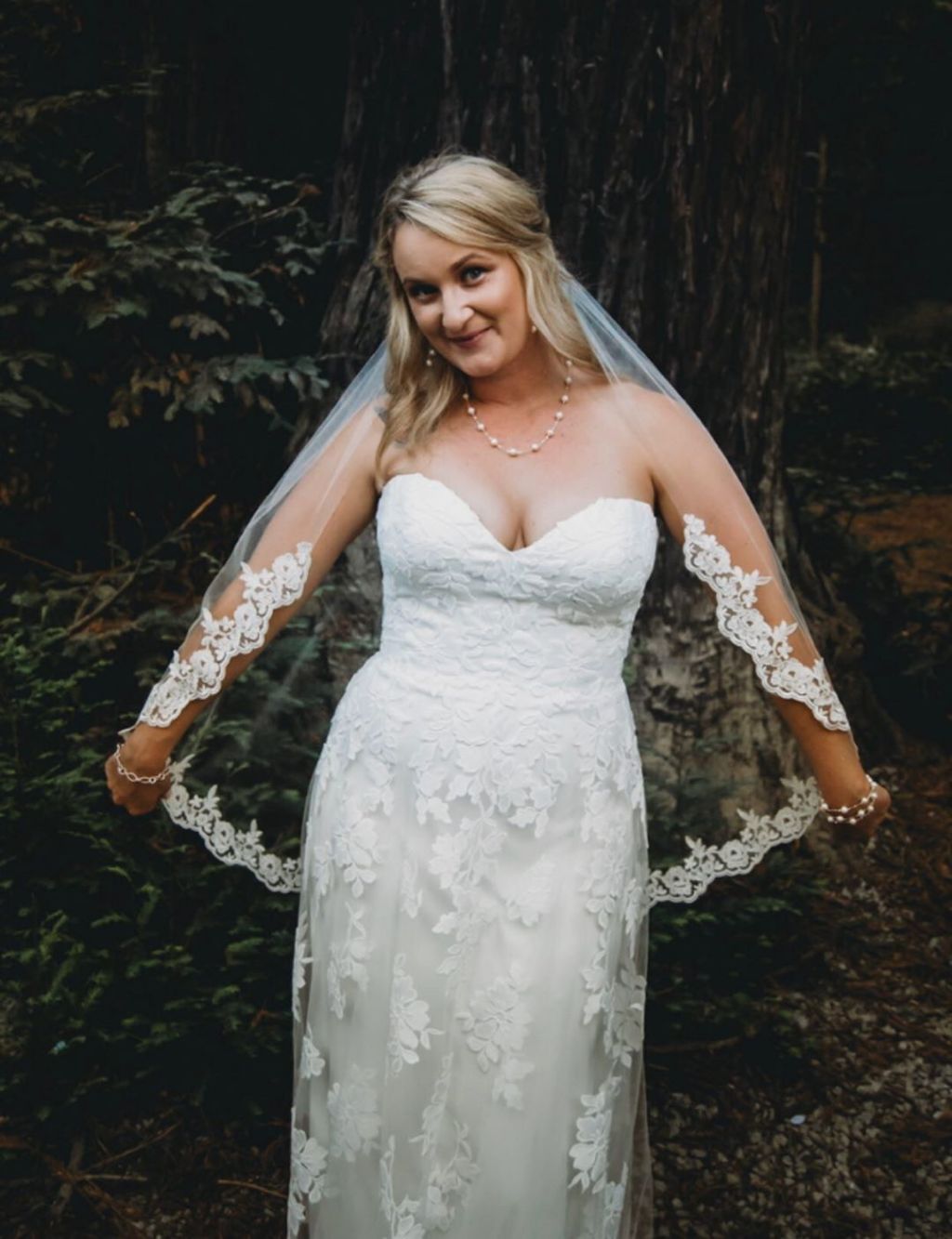 elegant semi lace edged fingertip length wedding veil on bride wearing sweetheart neckline strapless dress in the woods