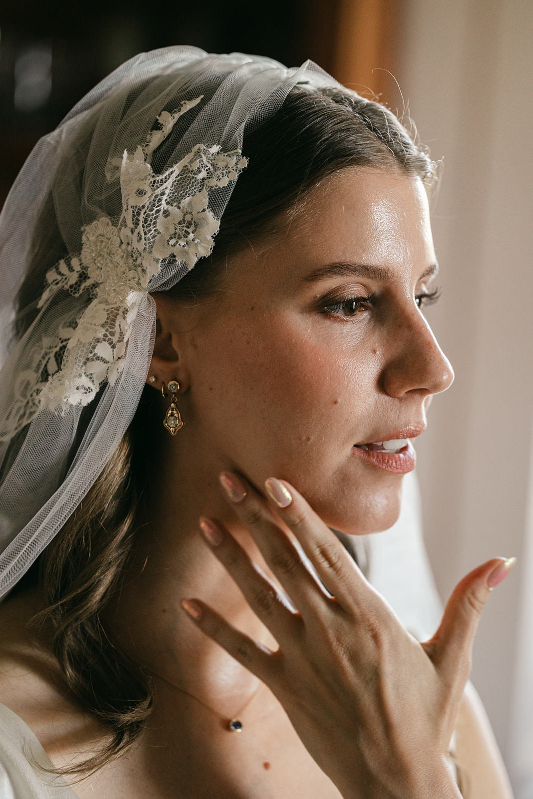 bride wearing a lace Juliet cap veil and earrings, with blush manicured nails