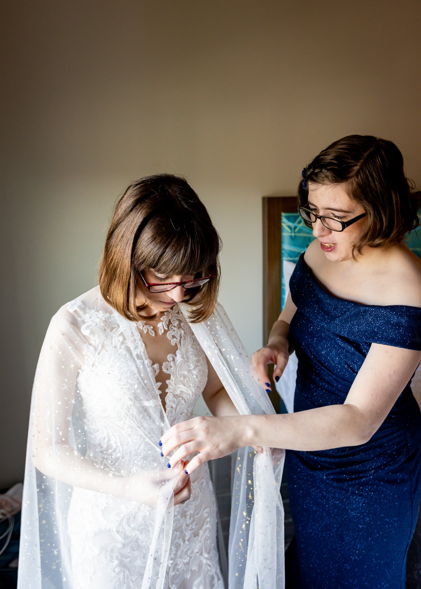 bridesmaid helping bride put on soft tulle bridal cloak over shoulders