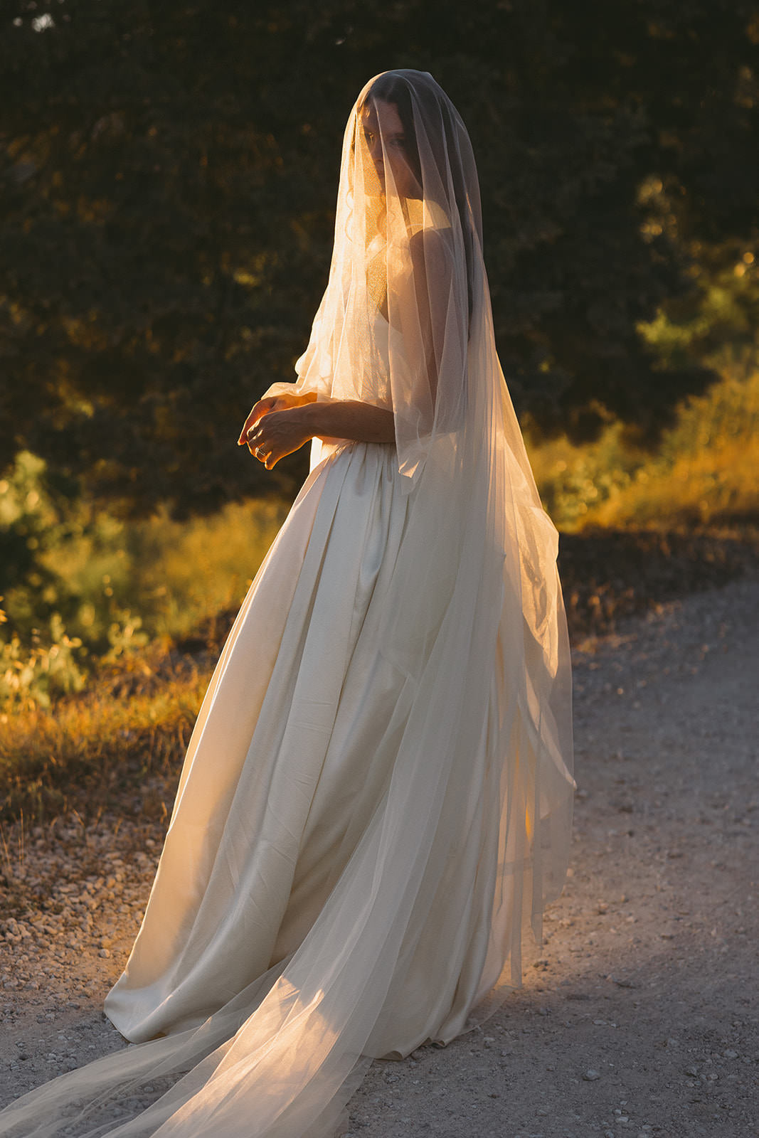 Woman in an ivory drop waist  Danielle Frankel wedding dress with a long silk drop cathedral veil standing on a dirt path with Italian greenery in the background.