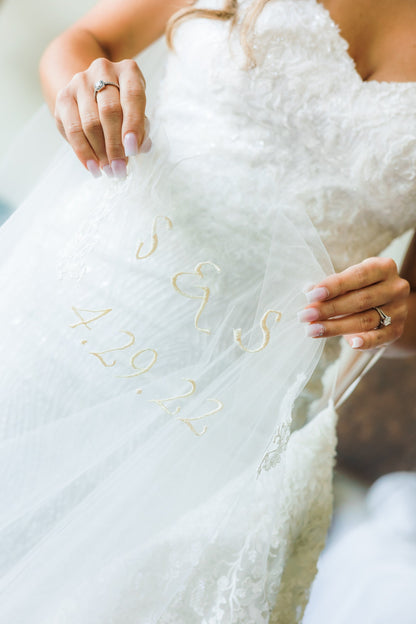 script cursive embroidery of couple's initials and wedding date written on bridal veil with bride holding it in hands