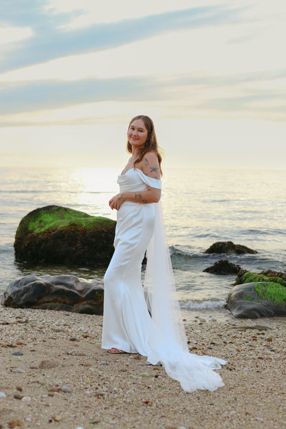 chapel length simple tulle bridal veil on bride in romantic off the shoulder draped gown standing on the sand