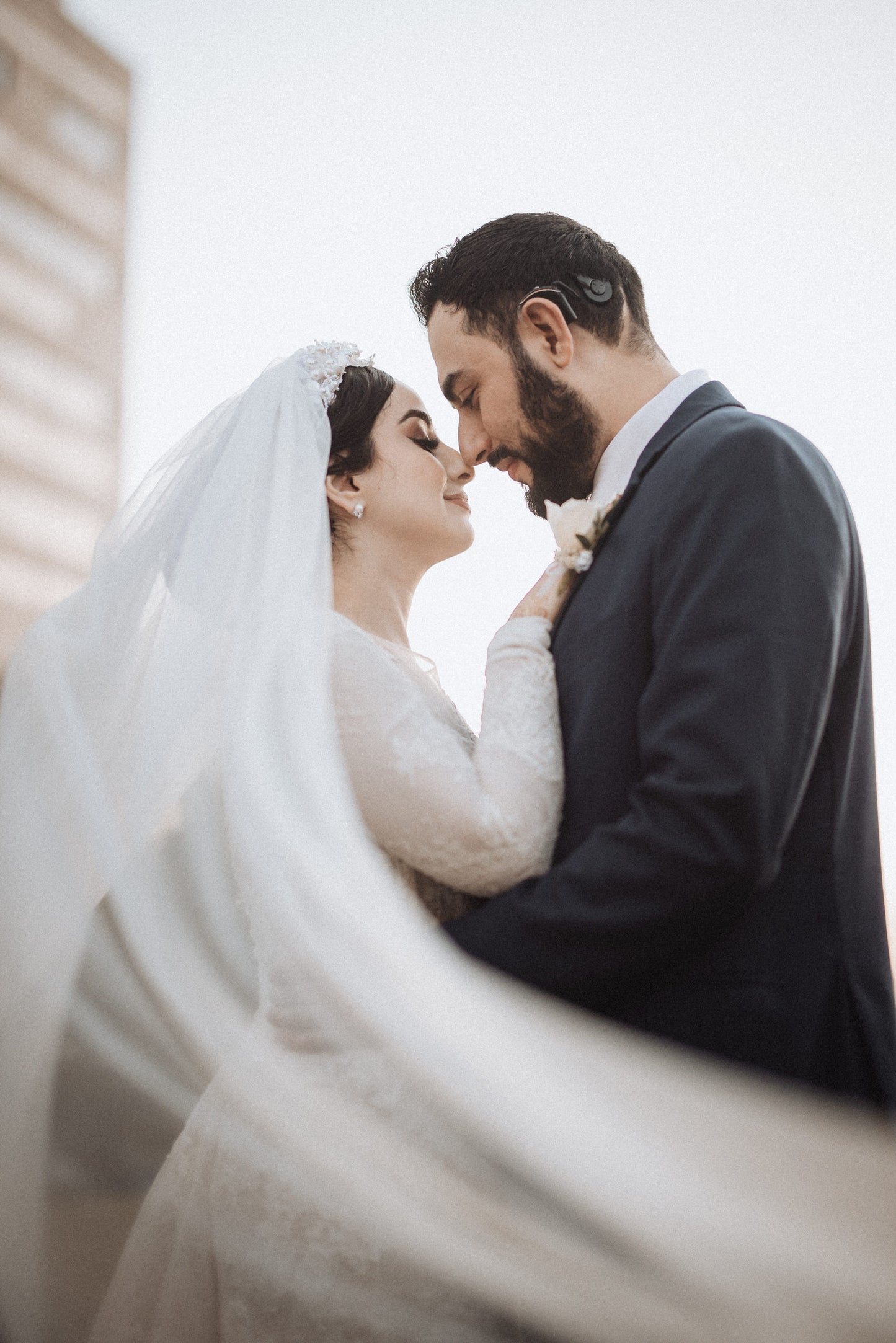 middle eastern bride in pearl bridal hat with scarf over updo and long tulle veil in wind