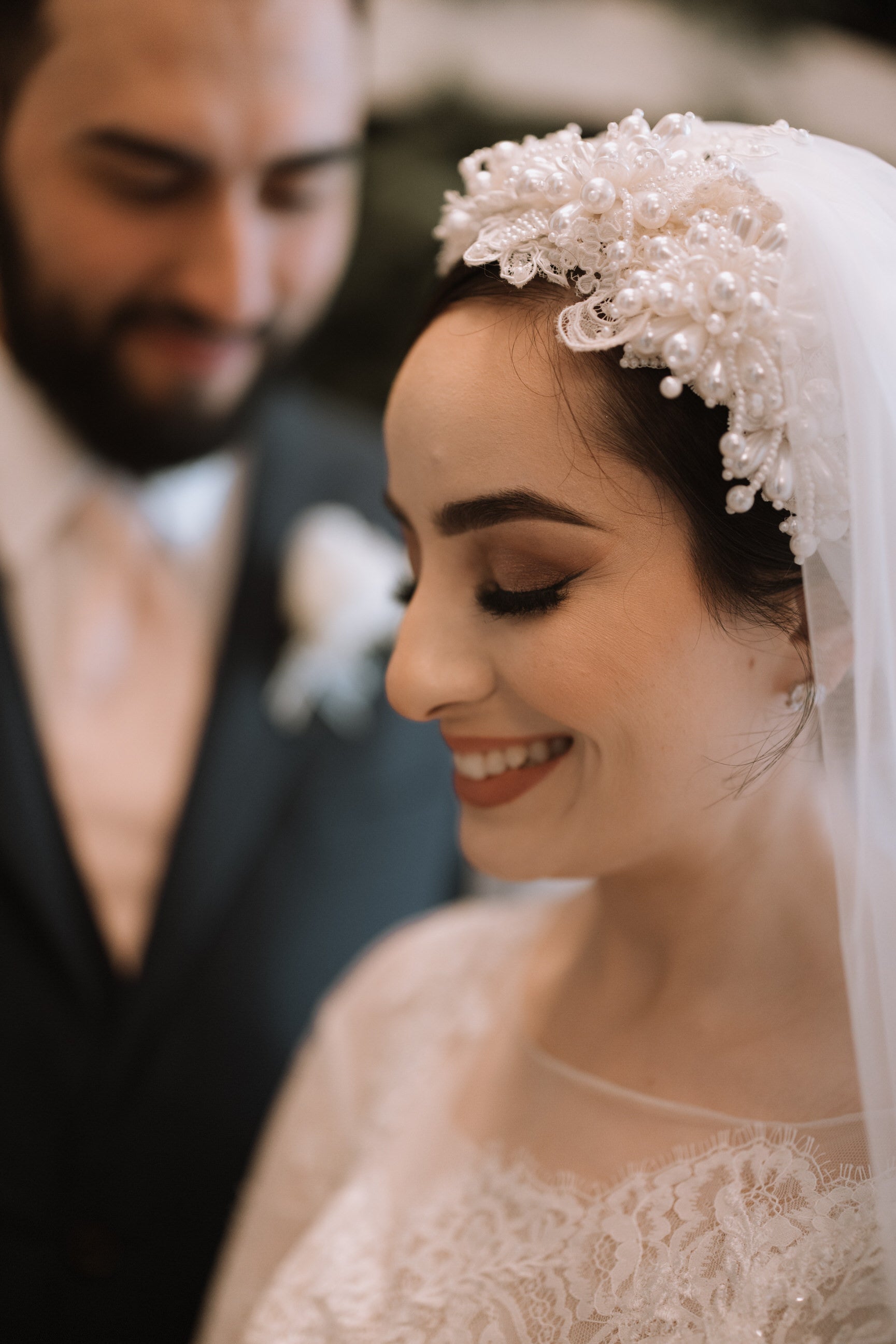romantic lace bridal turban with pearls and veil with groom in background