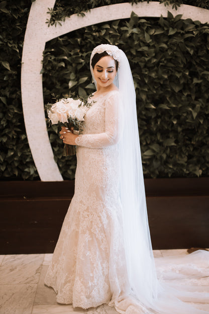 beautiful bride in ivory long sleeve gown wearing an bridal headband with long veil and bouquet of white roses