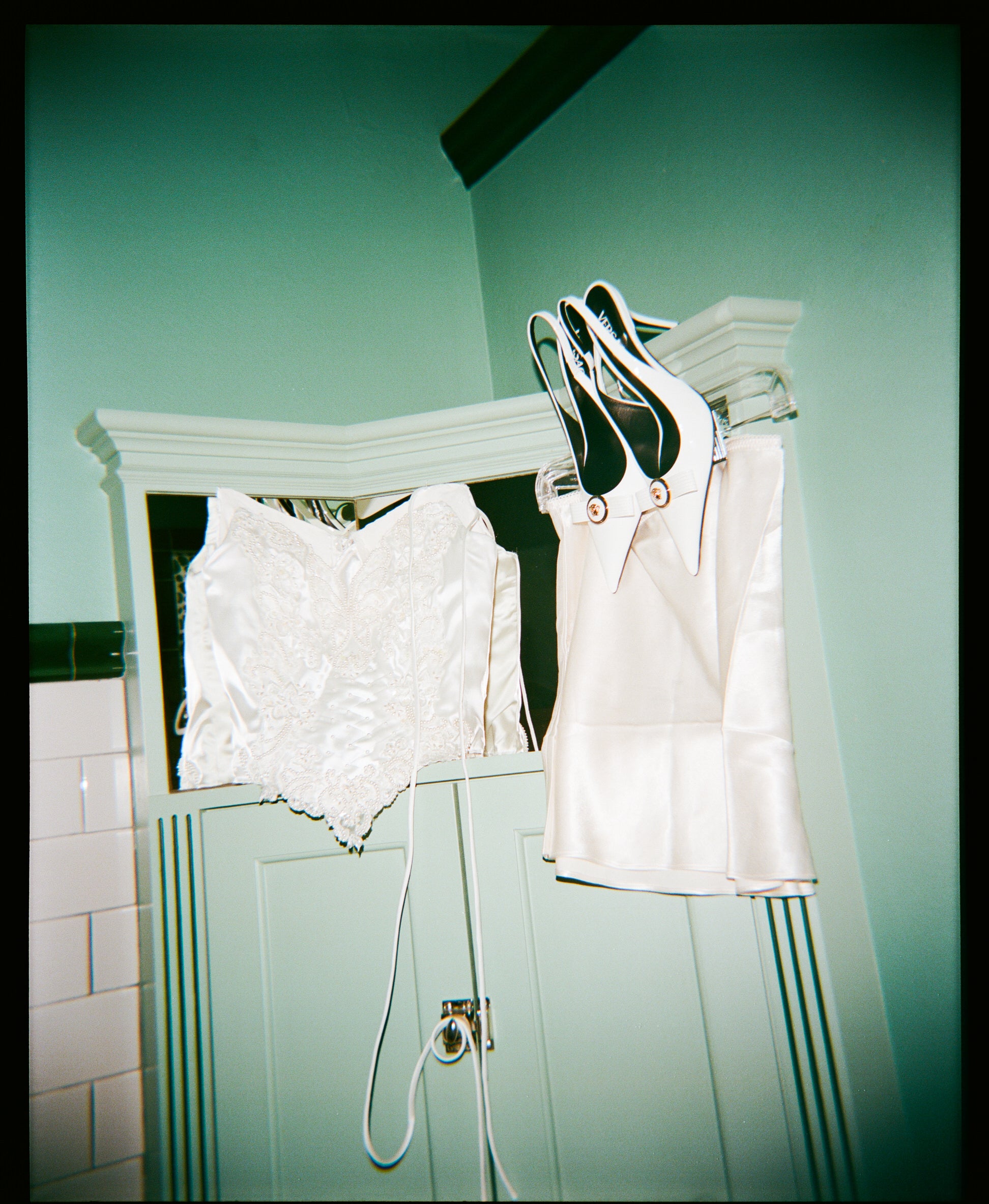 White lace and satin couture bridal corset bustier hanging on a rack against a teal wall.