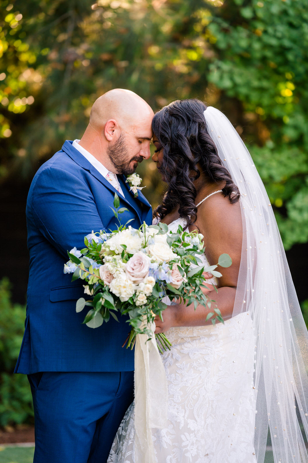 romantic bride and groom holding one another with bride wearing scattered pearl long white wedding veil and groom in navy blue suit