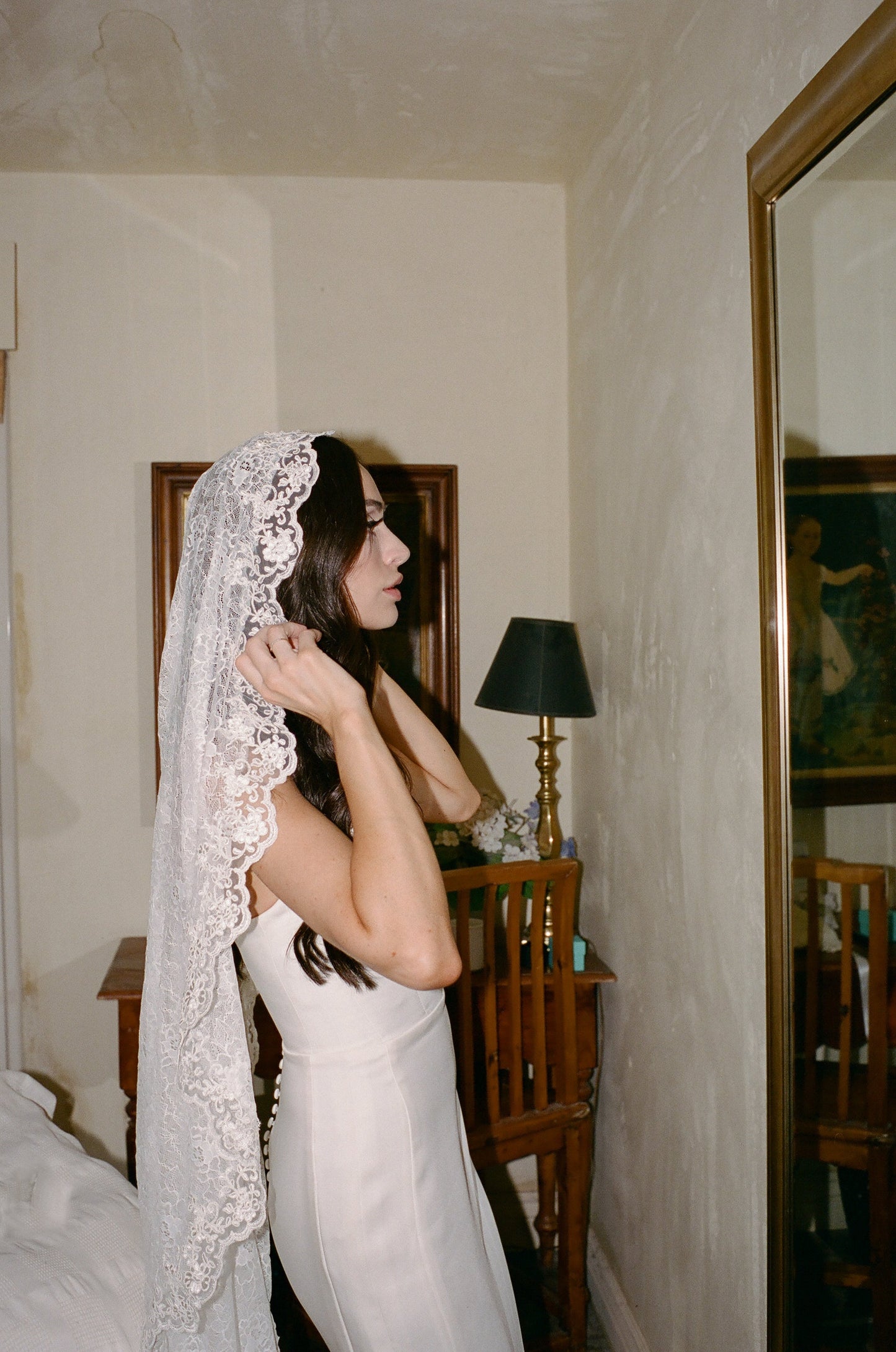 bride putting on her retro inspired mid length mantilla wedding veil in ivory color over long wavy hair