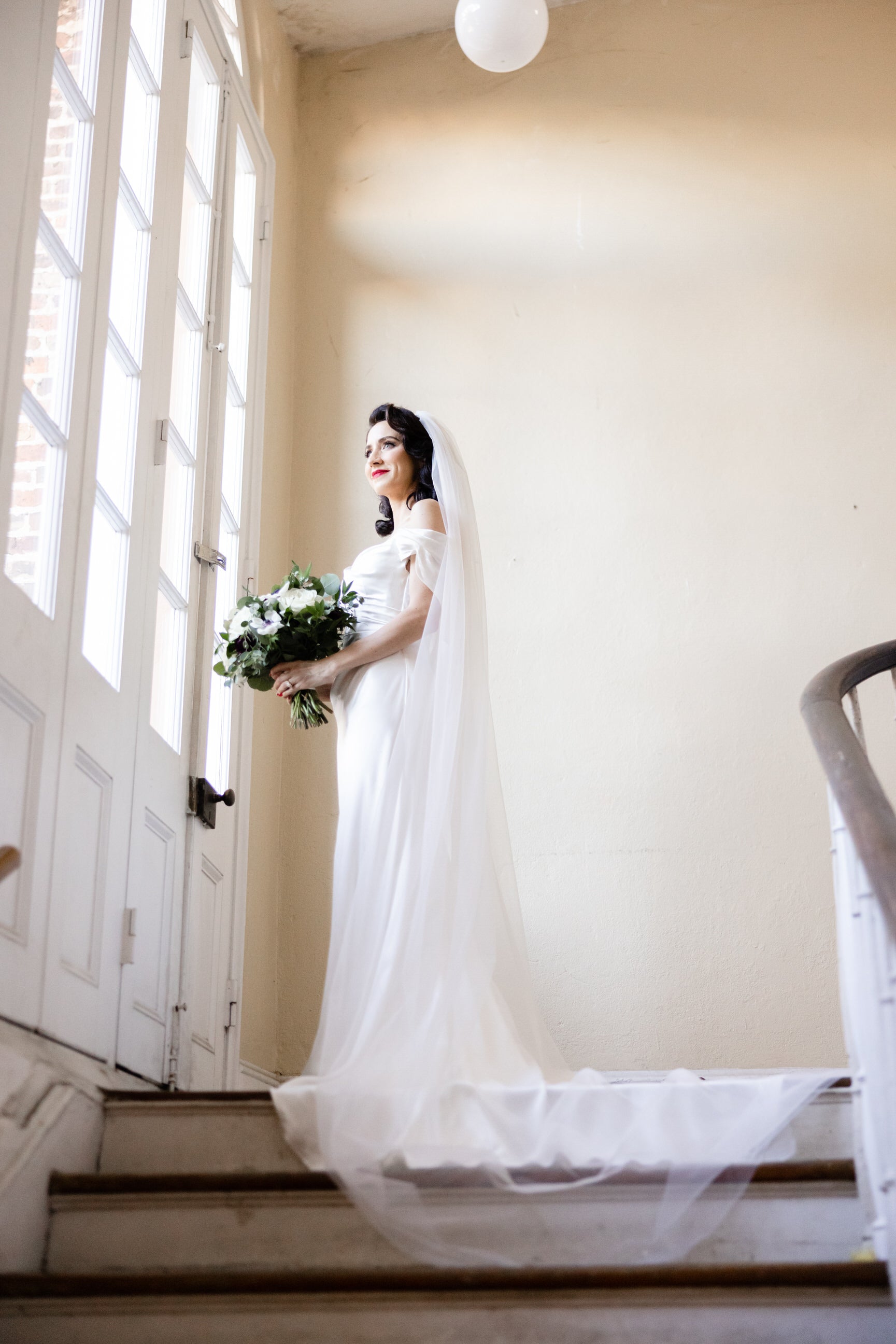 glam bride in soft silk net bridal veil with simple raw edge standing on staircase