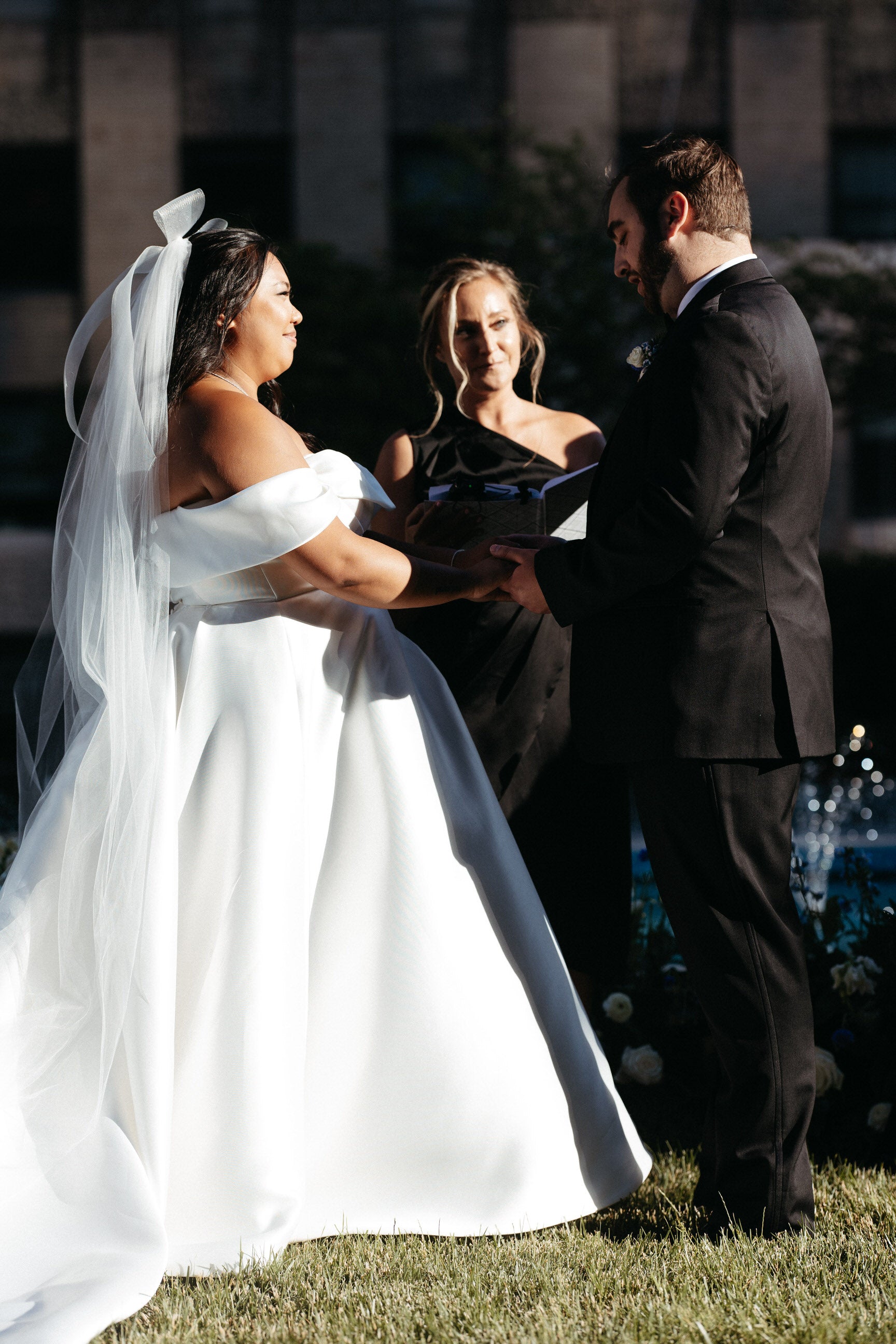 bridal hair bow with tails and long cathedral veil on bride saying vows in off the shoulder ballgown