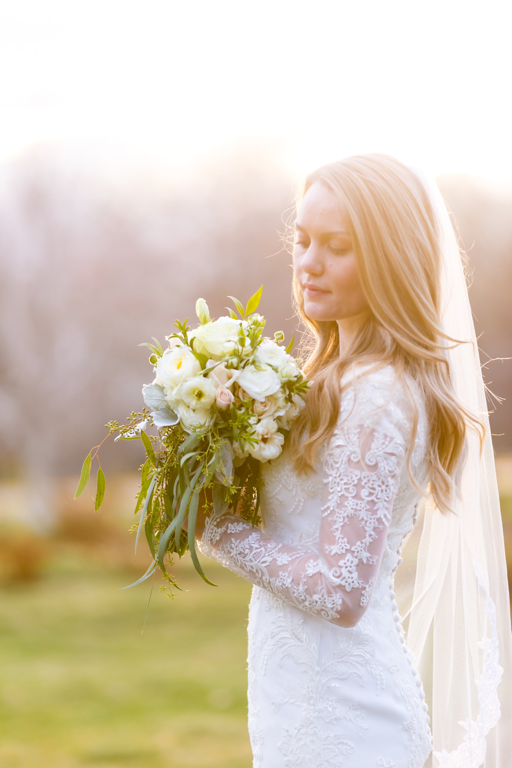 resort wedding with bride holding white bouquet with soft mid length lace bridal veil and long sleeved lace dress