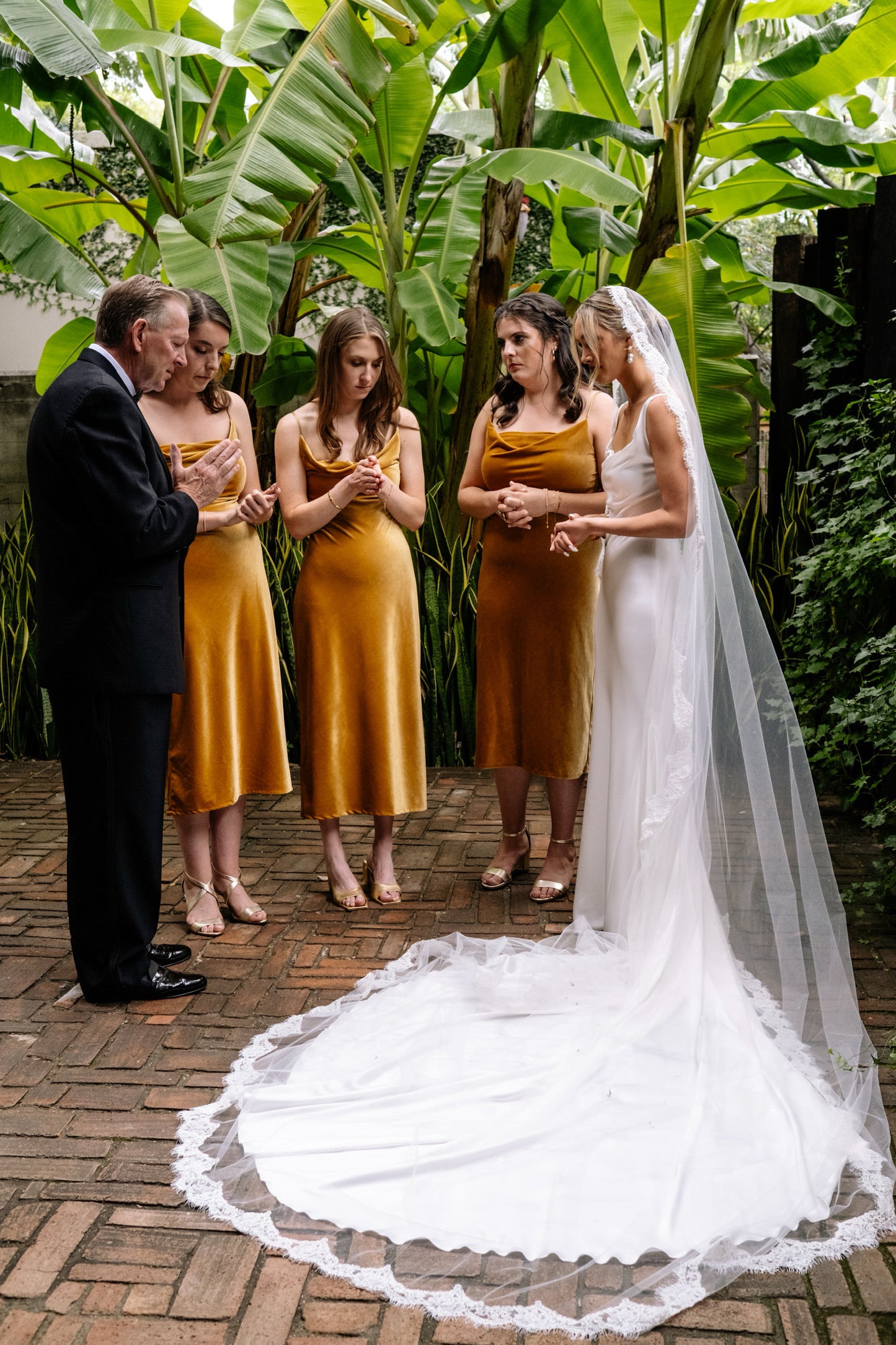 hacienda wedding as minimalist bride in long cathedral bridal veil with lace edge pray with the bridesmaids 