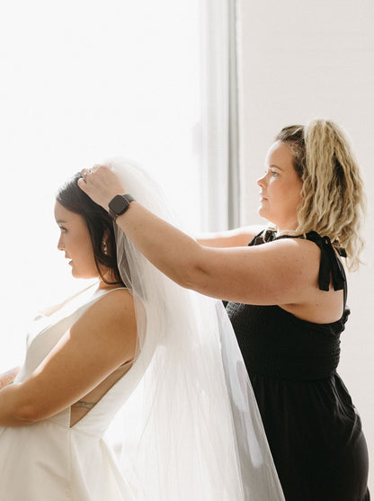 positioning wedding veil comb in curled hair as bride bends down for stylist
