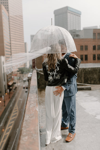 unique rooftop elopement with simple raw edge veil with embroidered names as couple stands beneath clear umbrella