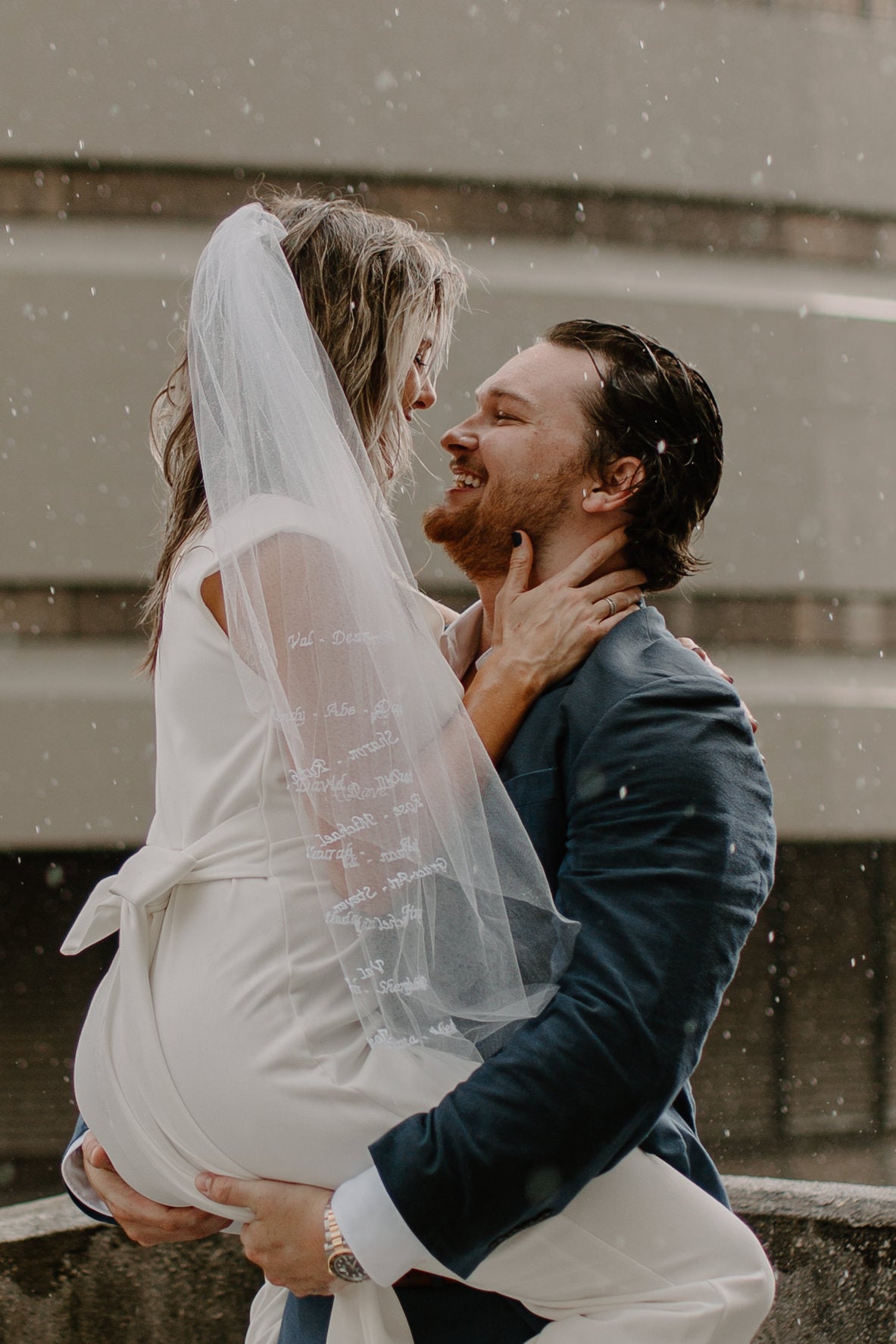 couple embracing in rain with bride in white sophisticated bridal veil wtih writing