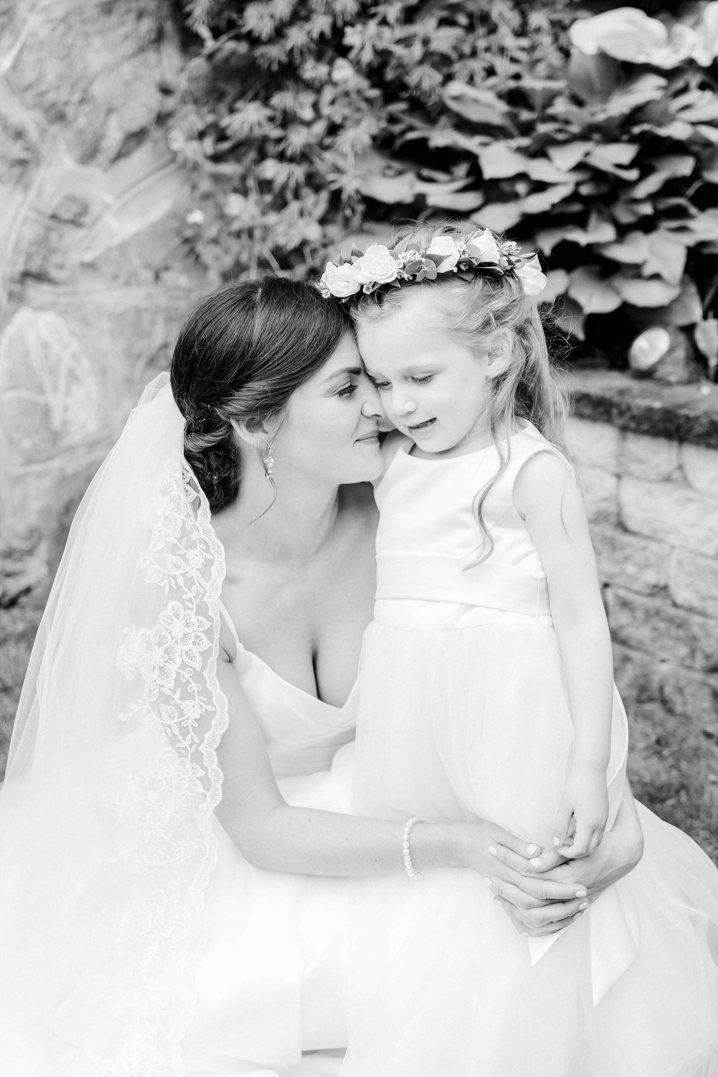 one blushing bride cathedral length lace bridal veil over low updo as bride embraces flower girl
