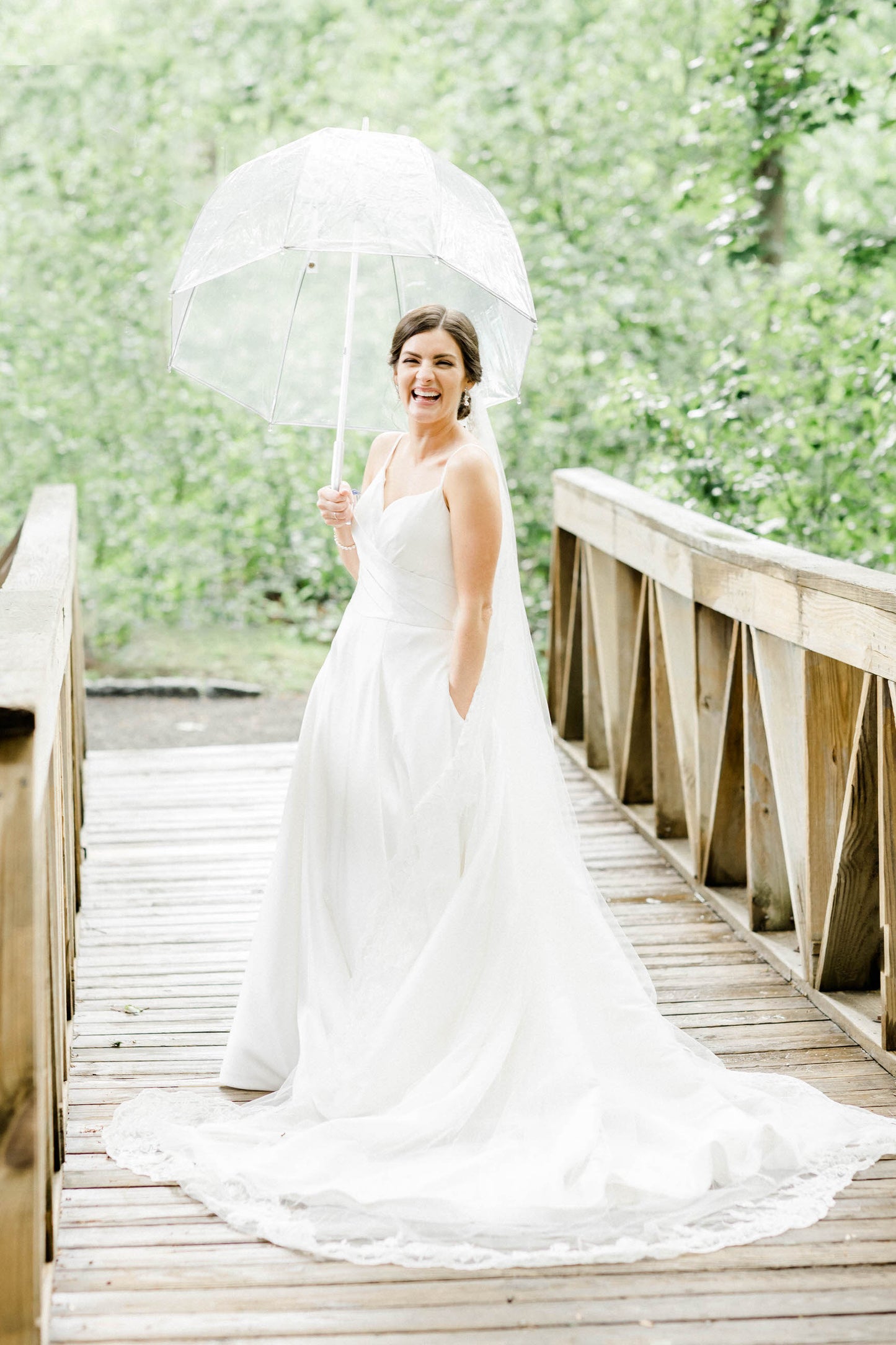 ballgown with pockets on bride wearing One Blushing Bride designer long cathedral length bridal veil with lace trim on bride under umbrella for rainy wedding day