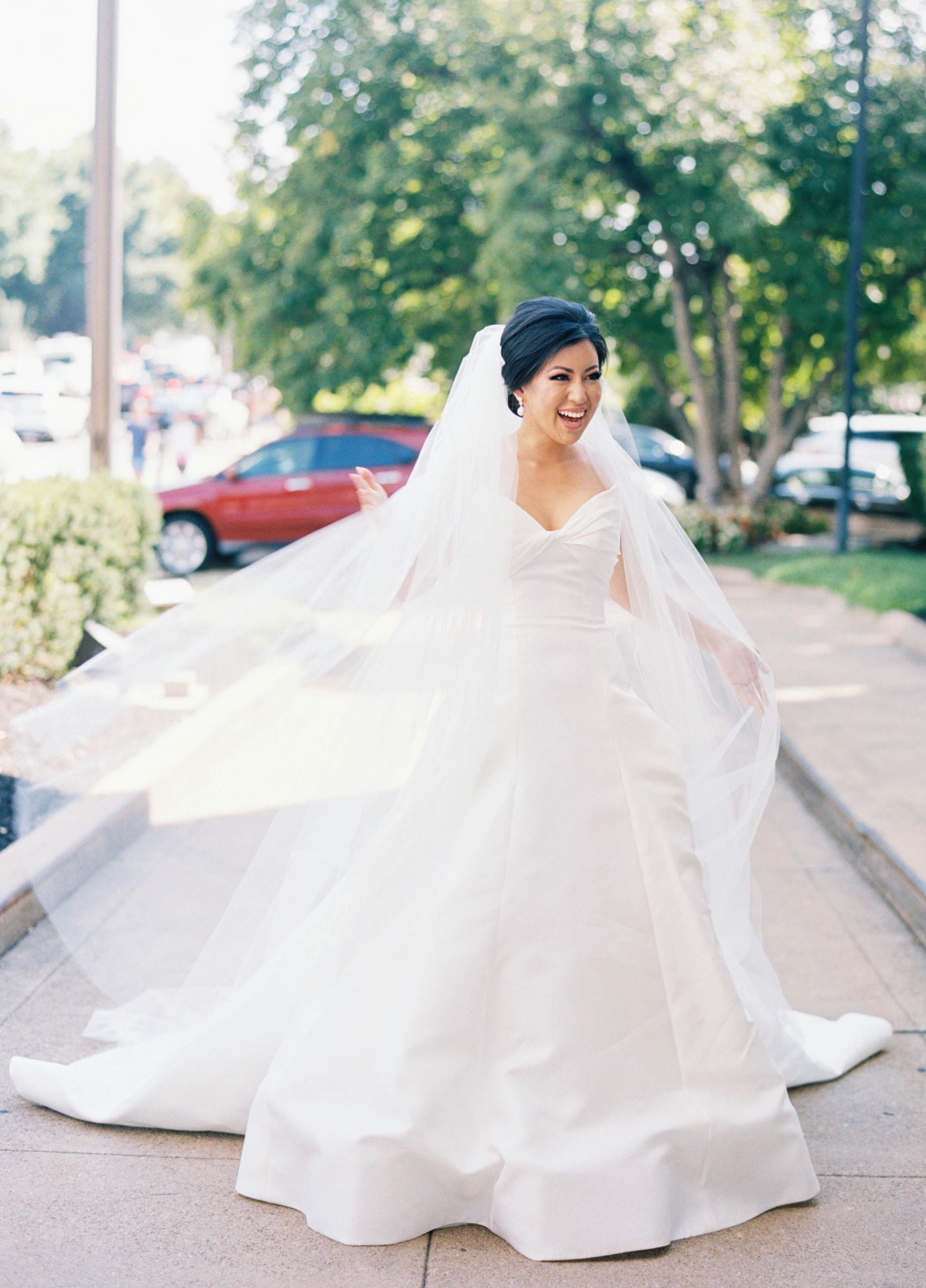 bride laughing as cathedral long white wedding veil blows 
