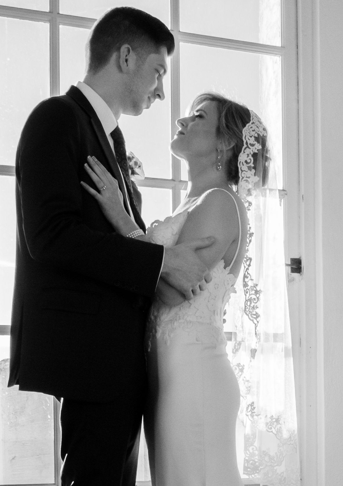 classy sheath style wedding dress with lace mantilla wedding veil as she looks up at groom 