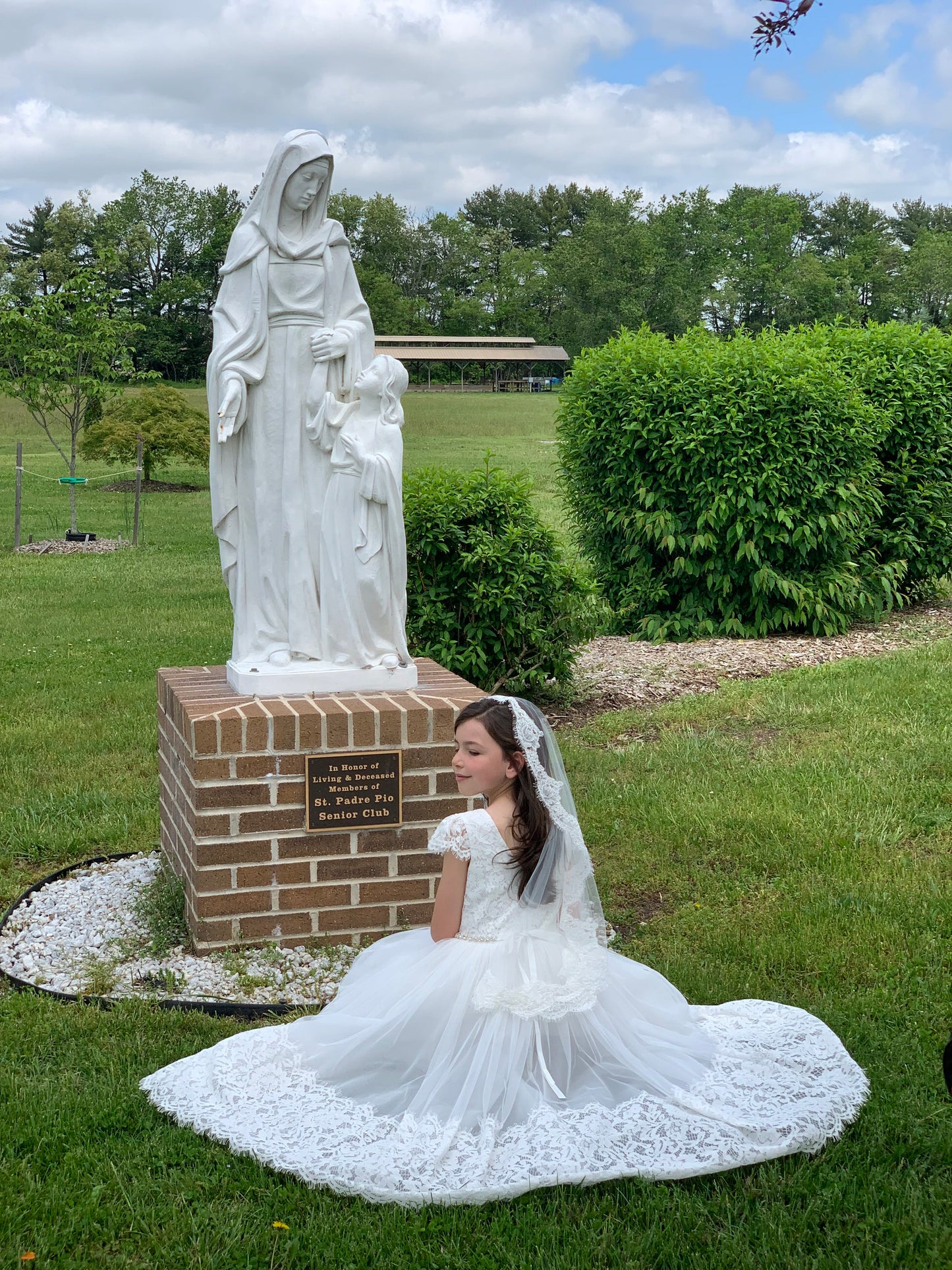 communion girl praying in front of Virgin Mary statue wearing lace edged communion veil in off white