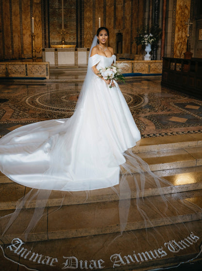 gold church wedding with bride wearing satin dress and extra long royal length veil with writing