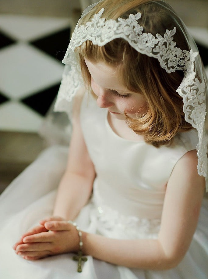 little girl praying wearing scallop lace edged communion veil before her first holy communion in church