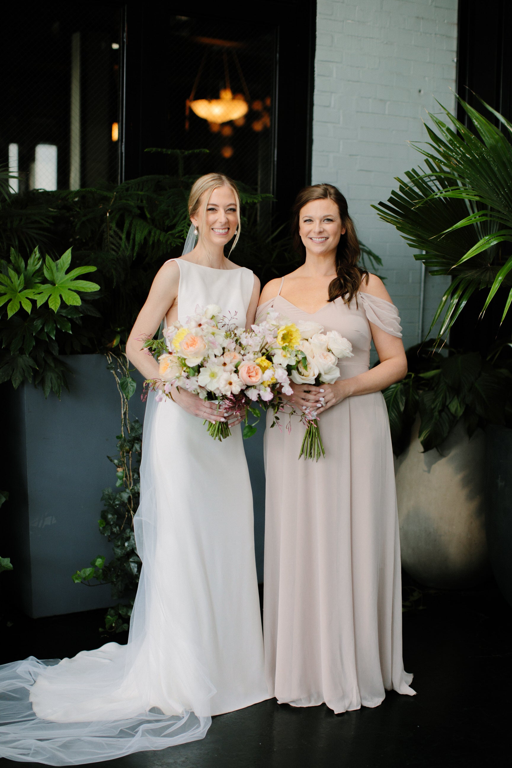 bride and bridesmaid with bride wearing off white cathedral length long soft wedding veil and boatneck crepe gown