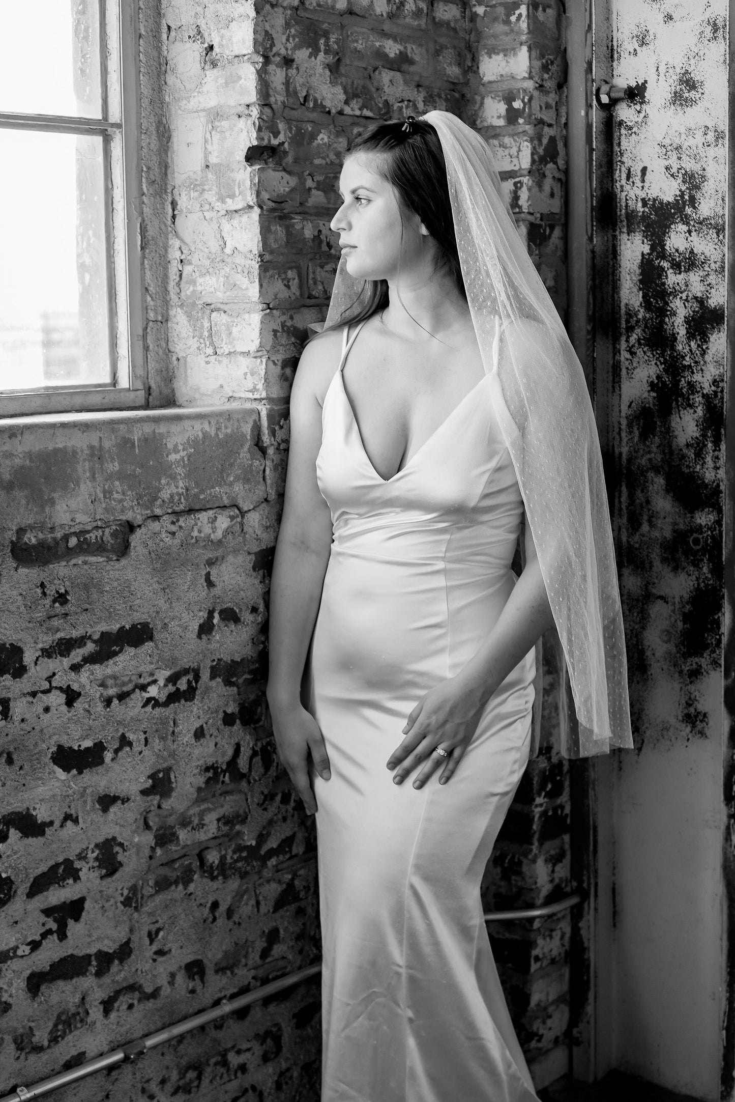 textured swiss dot polka dot fingertip wedding veil on bride in low neck V silk sheath wedding dress next to window