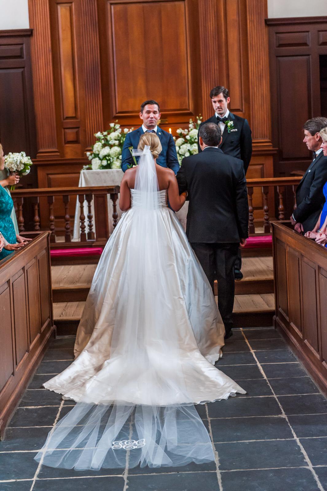 bride walking down church aisle in monogrammed cathedral veil
