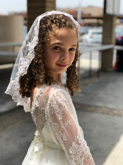 shoulder length first holy communion wedding veil on curly hair little girl wearing lace long sleeved dress with bow