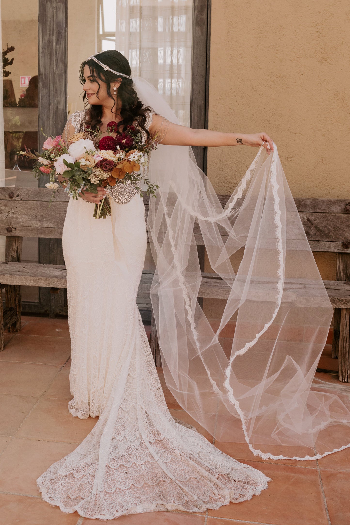 thin scallop wedding veil with eyelash edge starting at waist on bohemian Mexican bride holding burgundy and rust bouquet